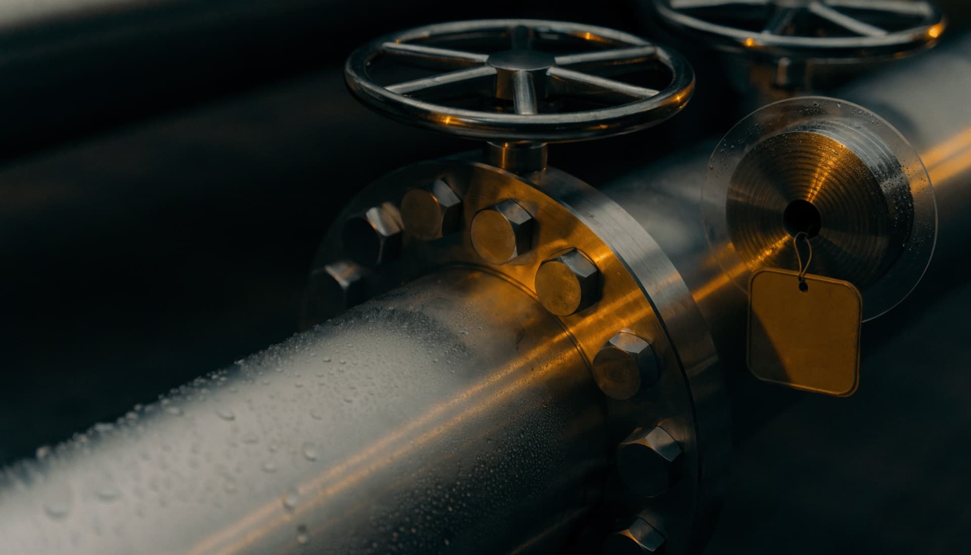 Close detail of a stainless steel pipeline manifold at a fuel terminal, valve handwheels and a sealed sampling point